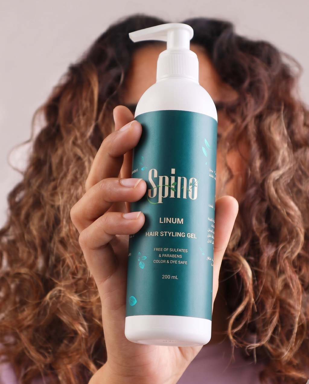 Person holding a bottle of Spino Linum hair styling gel with a blurred background