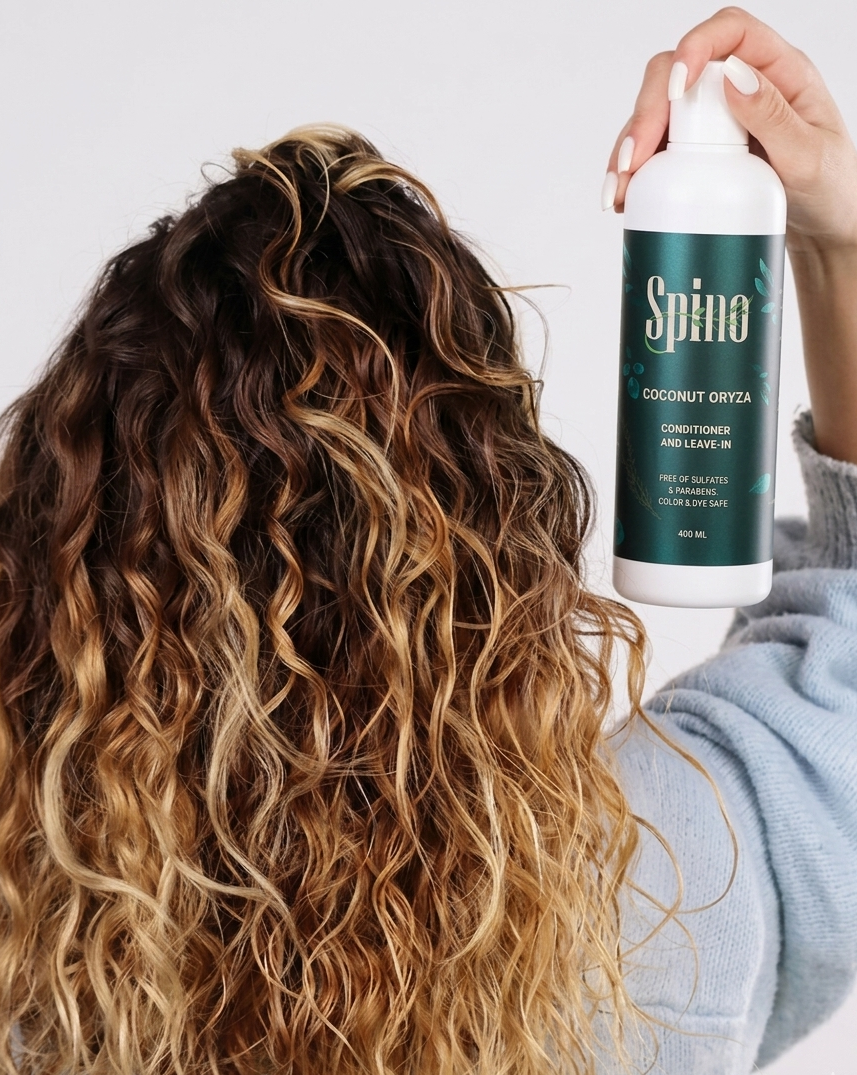 Person with wavy hair holding a bottle of Spino conditioner.